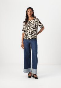 Leopardenprint top met korte mouwen, gecombineerd met wijde denim jeans met een lichtblauwe zoom. Zwarte hakken maken de outfit af.