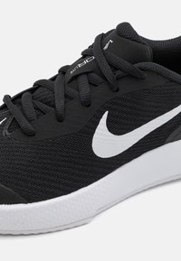 Čierna športová obuv s vrchnou časťou z sieťoviny, so znakem bieleho swoosh, plochými čiernymi šnúrkami a štruktúrovanou bielou gumovou podrážkou.