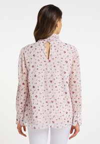 Lys pink blouse med små blomsterprint, høj halsudskæring og nøglehul-detail på ryggen. Lange ærmer med knaplukninger. Fremstillet af letvægtsstof.