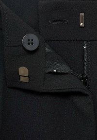 Černé kalhoty na míru s elegantním designem, zapínáním na knoflík, zipem a akcentem v doplňkové metalické barvě.