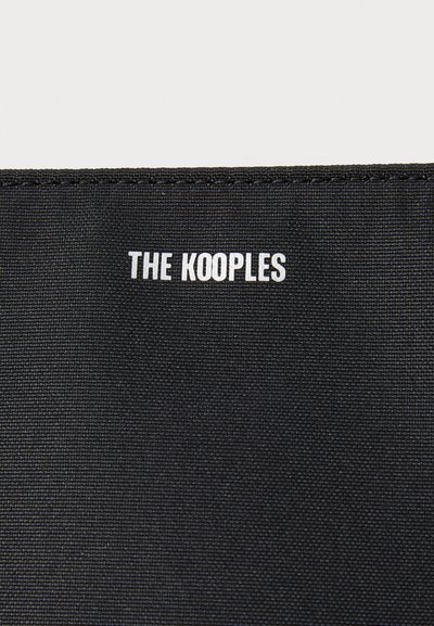 Musta kangaspussi, jossa on "THE KOOPLES" -logo valkoisena, sijoitettuna ylös keskelle. Pintamateriaali on sileä ilman lisäkuvioita tai -koristeita.