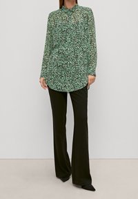 Blusa a maniche lunghe verde e nera con motivo, con colletto, abbinata a pantaloni neri a gamba dritta e scarpe nere a punta.