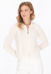 Crème-kleurige gebreide cardigan met een ritssluiting aan de voorkant, grote kraag en tekstuurpatronen langs de mouwen. Voorzien van geribbelde manchetten en zoom.