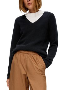 Zwarte geribbelde trui met V-hals, lange mouwen en een losse pasvorm, gecombineerd met lichtbruine broek met elastische taille in een gladde stof.