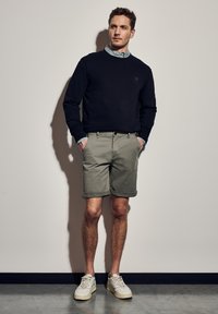 Námořnická mikina, světle kostkovaná košile pod ní, olivově zelené šortky a bílé tenisky. Neformální outfit s ohrnutými šortkami a volným střihem.