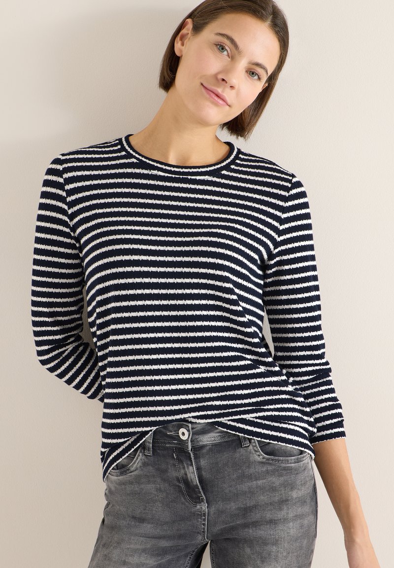 Suéter de manga larga con rayas marino y blancas, textura acanalada, escote redondo y corte holgado, combinado con jeans gris descoloridos.