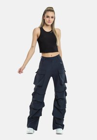 Navy cargo pants with multiple large pockets and a fitted waist, paired with a black cropped tank top. White sneakers complete the outfit.