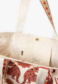 Sac en toile avec un intérieur beige, doté d'une poche zippée. L'extérieur présente un motif ludique de taches brunes et de cœurs sur fond blanc.