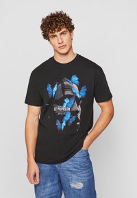 Sort bomulds T-shirt med grafik af blå sommerfugle og et ansigt. Rund hals, korte ærmer og afslappet pasform.