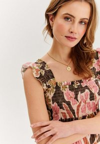 Šaty s kvetinovým vzorom, ktoré majú smockovaný dizajn, volánkové ramienka a farebnú paletu v odtieňoch ružovej, zelenej a hnedej.