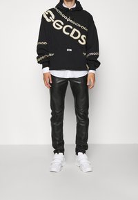 Felpa nera con logo bianco "GCDS" e design a catena, abbinata a pantaloni in pelle nera e sneaker bianche. Texture lisce, vestibilità casual.