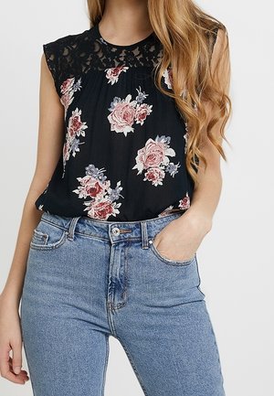 Blusa nera floreale con dettagli in pizzo sulle spalle, caratterizzata da motivi floreali rosa e blu. Abbinata a jeans in denim blu chiaro.