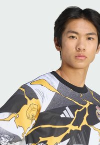 Camicia a maniche corte con un design grafico giallo brillante e nero, caratterizzata da un motivo crepato, scollo rotondo e tessuto strutturato.