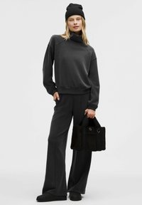 Grijze sweatshirt met een hoge kraag, bijpassende grijze wijde broekspijpen en een zwarte gestructureerde handtas. De outfit heeft een zachte stof en een ontspannen pasvorm.