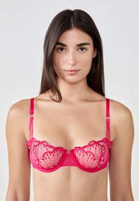 Różowa koronkowa biustonosz z przezroczystymi panelami, falbaniastymi krawędziami i delikatnymi detalami. Posiada regulowane ramiączka i gładki pas.