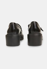 Fekete lakkbőr cipők lekerekített hátsó résszel és masszív fekete gumisarkakkal. Az elegáns dizájn és sima felület jellemzi őket.