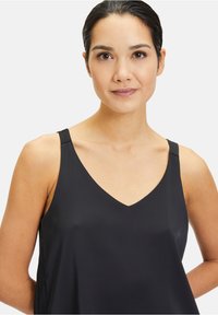 Zwarte mouwloze top met een V-halslijn en dunne schouderbanden, gemaakt van een gladde, lichte stof. Zachte val, minimale details.
