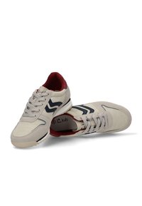 Zapatillas para niños en un beige claro con acentos en azul oscuro y interior rojo. Presenta un acabado texturizado, diseño con cordones y suela de goma.