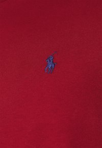 Röd bomullspolo med en blå broderad logotyp av en polo-spelare. Slät textur med ribbad krage och figurnära passform.