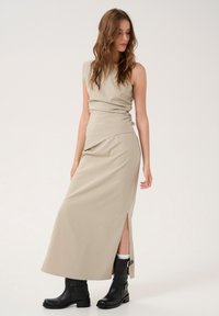 Beige sleeveless dress with a ruched bodice and a side split, paired with black leather ankle boots featuring buckles and a textured finish.