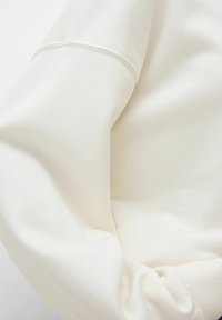 Felpa bianca con una texture morbida, caratterizzata da maniche lunghe e orli a coste. Il tessuto appare spesso e comodo, con dettagli di cucitura sottili.
