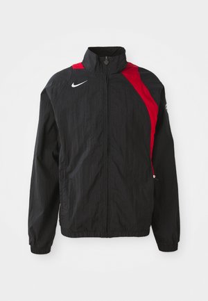 Schwarze Windjacke mit roten Akzenten, Reißverschluss, hohem Kragen, elastischen Bündchen und reflektierendem Logo-Detail auf der Brust. Leichtes, strukturiertes Material.