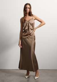 Robe nuisette en satin marron avec de la broderie décorative, dotée de fines bretelles et d'une silhouette fluide, assortie à des talons beiges pointus.
