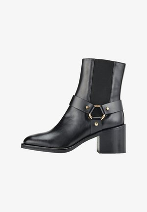 Bottine en cuir noir avec un talon rectangulaire. Elle présente des panneaux latéraux élastiques, une large bride ornée d'un anneau doré, et un bout pointu.