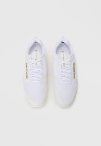 Baskets blanches de sport avec tige en mesh et synthétique, présentant des accents texturés, des lacets plats et un logo "SALMING" en doré.