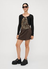 Crna majica dugih rukava s panelom od leopard uzorka, u kombinaciji s mini suknjom od smeđe umjetne kože. Model nosi debele crne platforme.
