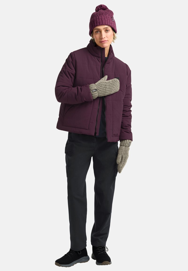 Bordeauxfarbene Steppjacke, gestrickte Mütze, graue strukturierte Handflächen, schwarze Hose und dunkle Sneakers. Die Jacke hat einen Reißverschluss und einen kastigen Schnitt.
