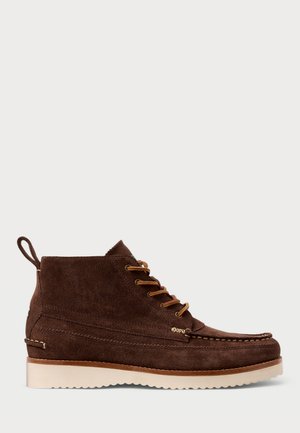 Botas de tobillo de ante marrón con una textura suave, que presentan acentos en color verde oliva, hardware dorado y una suela de goma ligera. Diseño de punta redondeada.