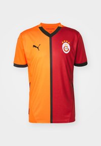 Galatasaray fodboldtrøje med orange og røde diagonale halvdele, sorte accenter, V-halsdesign og et Puma-logo på venstre bryst.