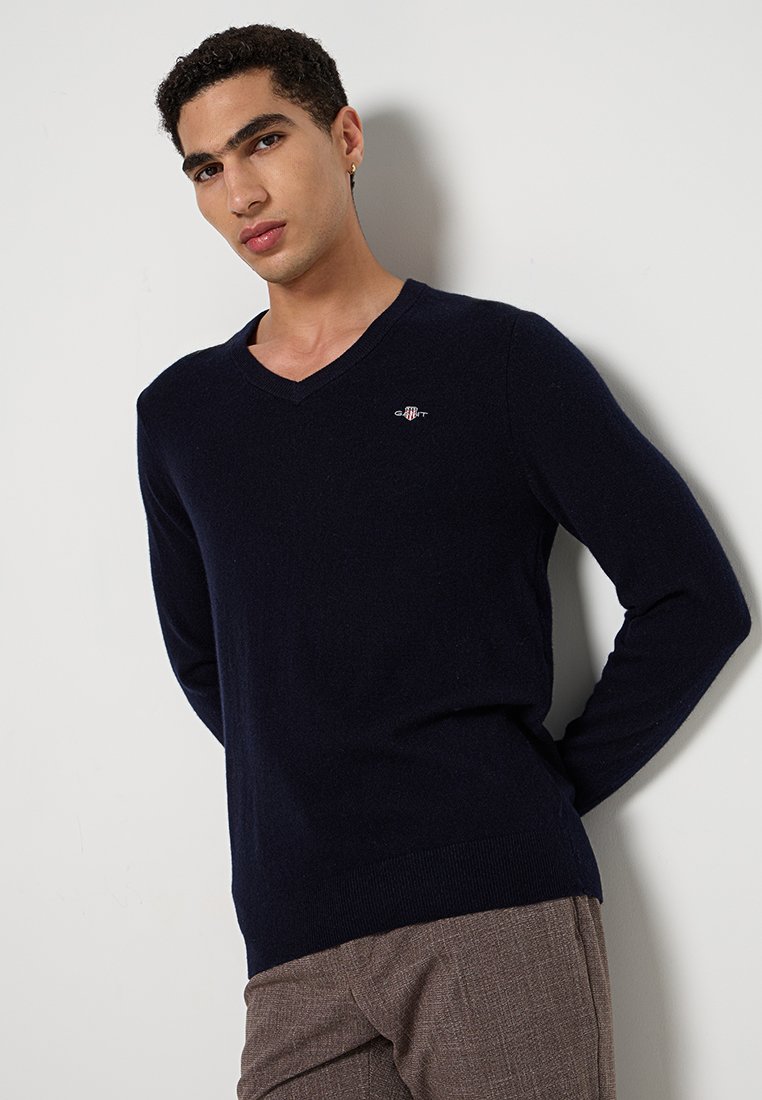 Marineblauer V-Ausschnitt-Pullover aus weichem Material mit gerippten Bündchen und Saum. Kleines Logo-Detail auf der Brust. Klassische Passform, leichte Textur.