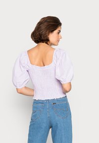 Top lilás de gingham com mangas bufantes e decote quadrado, corpete franzido e bainha desfiada, combinado com jeans de denim azul de cintura alta.