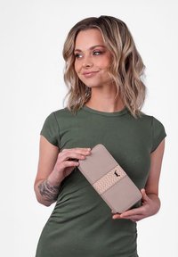 Beige wallet with a woven design and dark accents, held in a hand, featuring a smooth texture and rectangular shape.