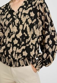 Blouse ample à imprimé animalier noir et beige, avec un décolleté en V, des poignets froncés et un ourlet élastiqué pour un effet texturé.