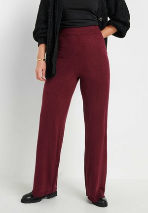 Bordeaux brede broek gemaakt van zachte stof met een elastische tailleband, gecombineerd met een zwarte oversized gebreide cardigan en zwarte laarzen.