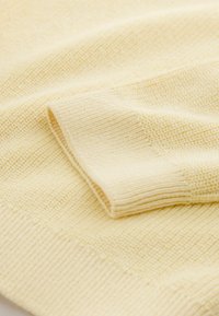 Gul strikket sweater med et tekstureret mønster og ribstrikkede manchetter og kant. Stoffet har et blødt, let udseende.