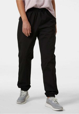 Pantalones de chándal negros y ligeros con cintura elástica y puños elásticos. Combinados con zapatillas grises, que tienen una textura suave y un corte relajado.
