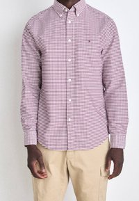 Camicia a quadri rossa e bianca con colletto classico, maniche lunghe e chiusura a bottoni. Presenta un motivo a quadri contrastanti.