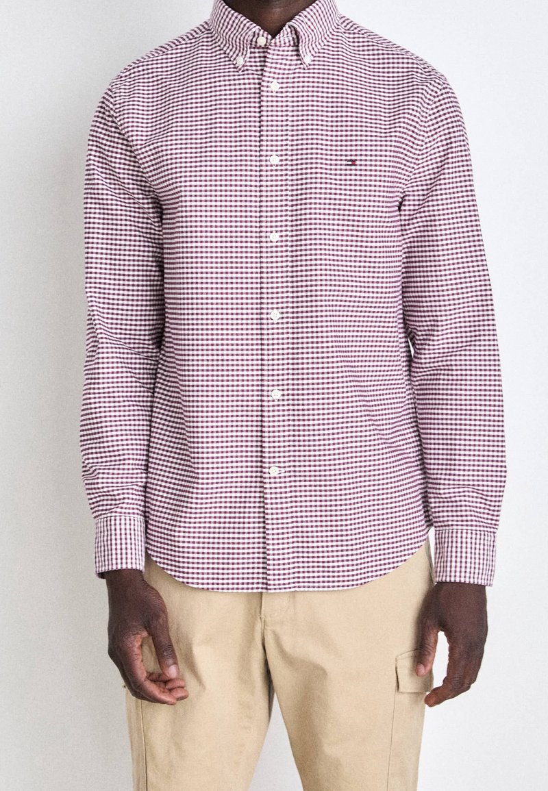 Camicia a quadri rossa e bianca con colletto classico, maniche lunghe e chiusura a bottoni. Presenta un motivo a quadri contrastanti.