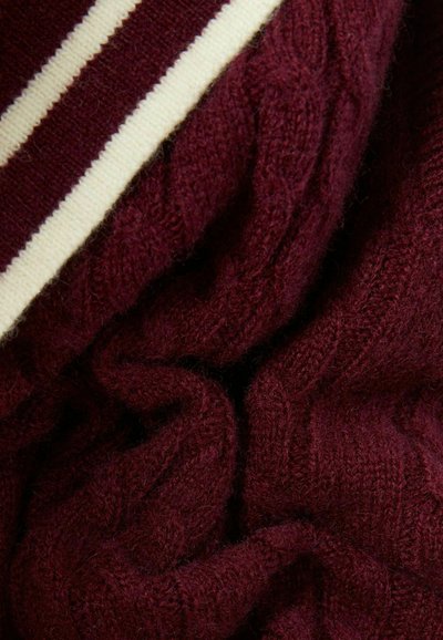 Tejido de suéter de punto burdeos con un patrón de trenzas y un cuello a rayas blancas. Presenta una textura suave y una apariencia drapeada.