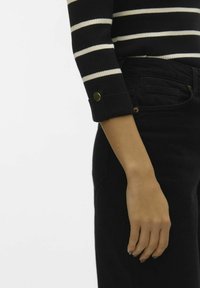 Mustvalge triibuline sviiter, ribatekstuuriga, millel on rullpocketil kuldne nööp, koos kõrge vöökohaga mustade teksadega.