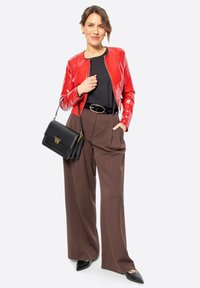 Veste en cuir rouge ajustée, haut noir, pantalon taille haute marron, ceinture noire et sac à main noir avec une touche dorée. Chaussures noires pointues.