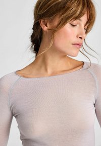 Hellgraues Langarm-Oberteil mit weitem Ausschnitt und Raglanärmeln, das eine glatte Textur und kontrastierende Nähte entlang der Kanten aufweist.