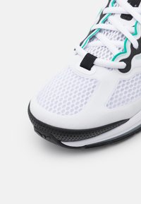 Vit sportskor med överdel i mesh, svart sula och turkosa detaljer. Har platta snören och perforerade inslag för andningsförmåga.