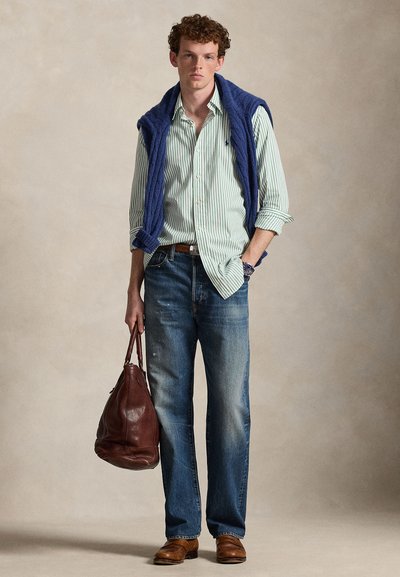 Light green and white striped button-up shirt, navy sweater draped over shoulders, blue jeans, brown leather belt, brown bag, brown shoes.