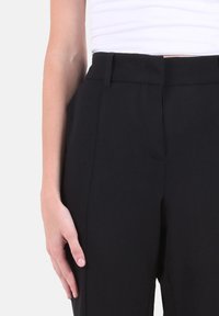 Pantaloni neri su misura con una texture liscia, caratterizzati da un davanti piatto, tasche laterali e pieghe sottili per una silhouette pulita.