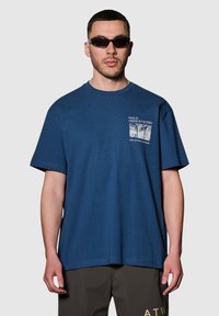 Mörkblå bomullströja med lös passform, rund halsringning och korta ärmar. Har en grafisk tryck på vänster bröstområde.